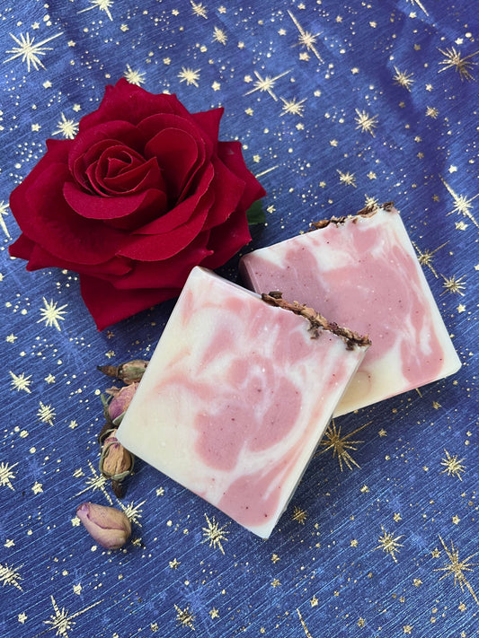 Pink and cream bars of soap next to red rose and small rose buds against blue fabric with gold stars